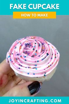 someone holding up a cupcake with pink frosting and sprinkles on it