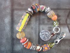 THIS IS A COLORFUL AUTHENTIC VENETIAN MILLEFIORI BEADS BRACELET WITH A YELLOW, RED AND ORANGE LARGE FOCAL BEAD (29 MM) . NEXT TO IT IS A BRASS WHEEL BEAD AND 2 OTHER AFRICAN SLICES. THE SILVER SPACERS ARE TIBETAN AND THERE IS A SMALL CHIC ON THE ORANGE AFRICAN END BEAD. TWO TURKISH BLOWN GLASS BEADS ADD MORE COLOR TO THE SCHEME. AT THE JUMP RING IS AN 18 MM SILVER PLATED CHARM OF A DEER. THERE IS  ALSO A CORAL RONDELLE, AND A YELLOW CLEAR BEAD WITH YELLOW GLASS SPRINKLES. ALL IN ALL A UNIQUE AND Artisan Yellow Bracelets With Round Beads, Unique Yellow Festival Bracelets, Orange Bohemian Bracelets With Spacer Beads, Bohemian Yellow Jewelry With Spacer Beads, Bohemian Yellow Round Beads Bracelets, Bohemian Hand-strung Yellow Bracelet, Yellow Bohemian Beaded Bangle Bracelet, Bohemian Yellow Hand-strung Bracelet, Eclectic Multicolor Bracelet With Spacer Beads