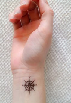 a small compass tattoo on the left wrist and right hand is shown in black ink