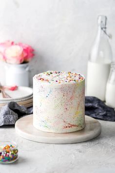 a white cake with sprinkles sitting on top of a table next to a bottle