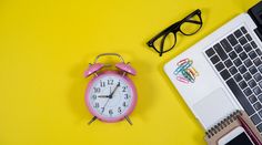 a pink alarm clock sitting on top of a laptop computer next to a pair of glasses