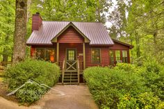 a small red cabin in the woods surrounded by trees and bushes, with stairs leading up to it