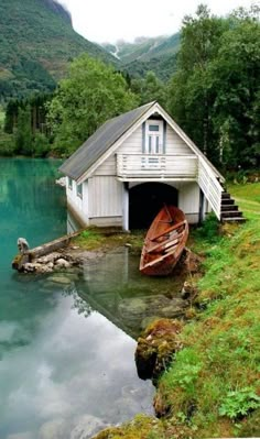 a boat sitting in the water next to a small house with a dock on it