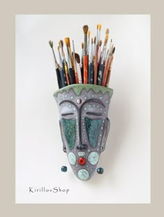 a ceramic mask with lots of paint brushes sticking out of it's mouth and eyes