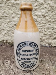 a white and brown bottle sitting on top of a cement ground next to a wall