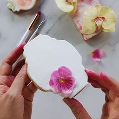 a person holding a piece of cake with pink flowers on it next to other decorated cookies