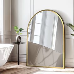 a mirror sitting on top of a wooden floor next to a bath tub and window