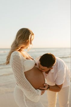 a pregnant couple kissing on the beach at sunset