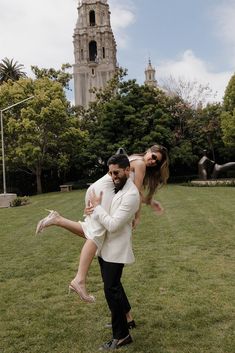 a man holding a woman on his back in front of a building with a clock tower