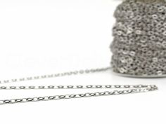 a roll of silver colored chain on a white surface with a spool of thread next to it