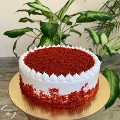 a red velvet cake with white frosting on a gold plate next to a potted plant