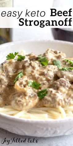 a white plate topped with pasta covered in meat and gravy next to a bottle of wine