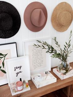 three hats are hanging on the wall next to two pictures and a vase with plants