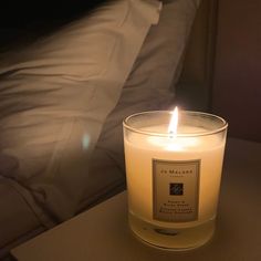 a lit candle sitting on top of a table next to a bed with white sheets