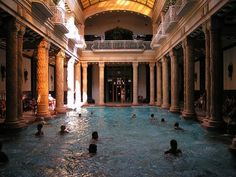 people are swimming in an indoor pool surrounded by columns