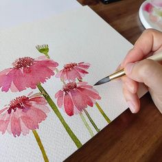 a person is painting pink flowers on white paper with a brush and watercolor pencil