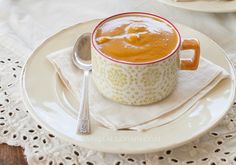 a bowl of soup on a plate with a spoon next to it and a lace doily