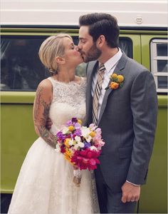 a bride and groom kissing in front of a green bus