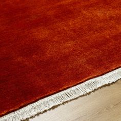 an orange rug with white fringes on top of it and a wooden floor in the background