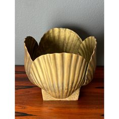 two gold shell shaped bowls sitting on top of a wooden table next to a gray wall