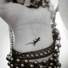 a small lizard tattoo on the left side of the wrist, with beads around it