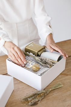 a woman is opening a gift box on a wooden table with dried herbs in it