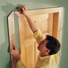 a man in yellow shirt holding up a wooden door frame to the wall with his hands