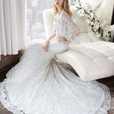 a woman in a wedding dress sitting on a white couch next to a large window