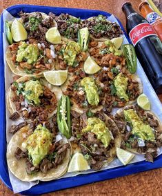 an assortment of tacos and beer on a blue tray next to a soda bottle