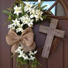 a wreath with white flowers and a cross on it is hanging from the front door