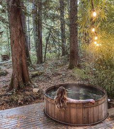 a woman in a wooden hot tub surrounded by trees