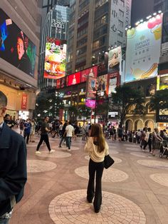 a woman standing in the middle of a plaza surrounded by tall buildings and lots of people