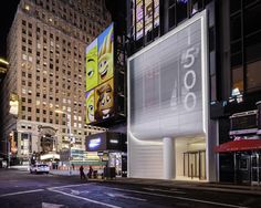 an empty city street at night with tall buildings and billboards on the building's side