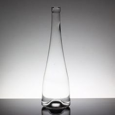 a clear glass bottle sitting on top of a reflective surface in front of a white wall