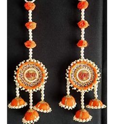 two orange and white earrings hanging from a black wall with beads on it's sides