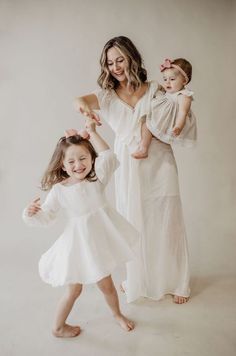 a mother and her two daughters posing for the camera in their white dresses, with one holding