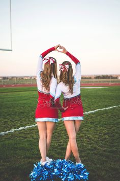 two cheerleaders standing in the middle of a field with their hands on their heads