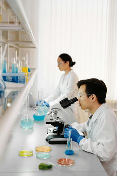 two people working in a lab with blue liquid on the counter and one person looking through a microscope