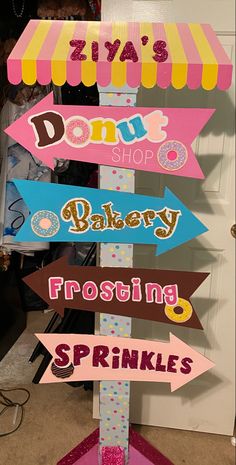 a sign that has some signs on it in the shape of a donut shop, bakery, frosting sprinkles and donuts