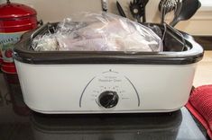 a white and black crock pot sitting on top of a counter next to utensils