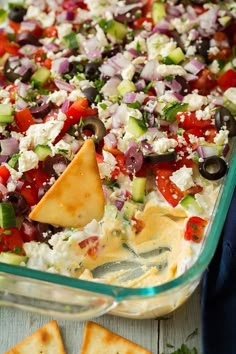 an image of a layered greek dip in a casserole dish with tortilla chips