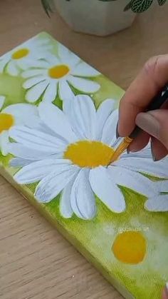 someone is painting daisies on a piece of green paper with yellow and white paint