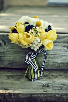 a bouquet of yellow and white flowers sitting on top of a wooden bench next to a black ribbon