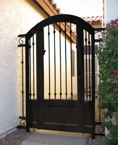 an iron gate is open on the side of a house in front of a pink flower bush