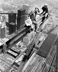 two people sitting on the edge of a tall building