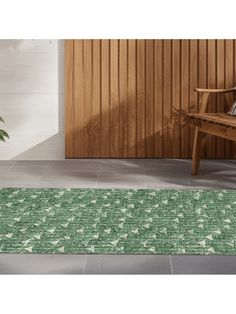 a green rug on the floor in front of a wooden wall and bench with a potted plant next to it