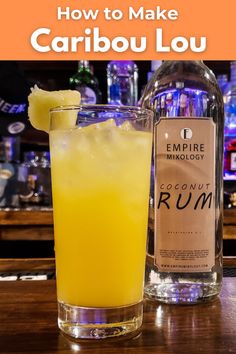 a glass filled with yellow liquid next to a bottle of alcohol on a bar top