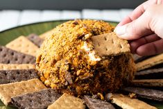 a person dipping crackers into a cheese ball on a plate with crackers around it