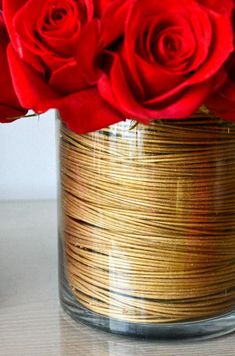 red roses are in a glass vase with gold wire wrapped around the bottom and sides