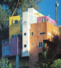 a multi - colored building with balconies and windows on the top floor is surrounded by trees